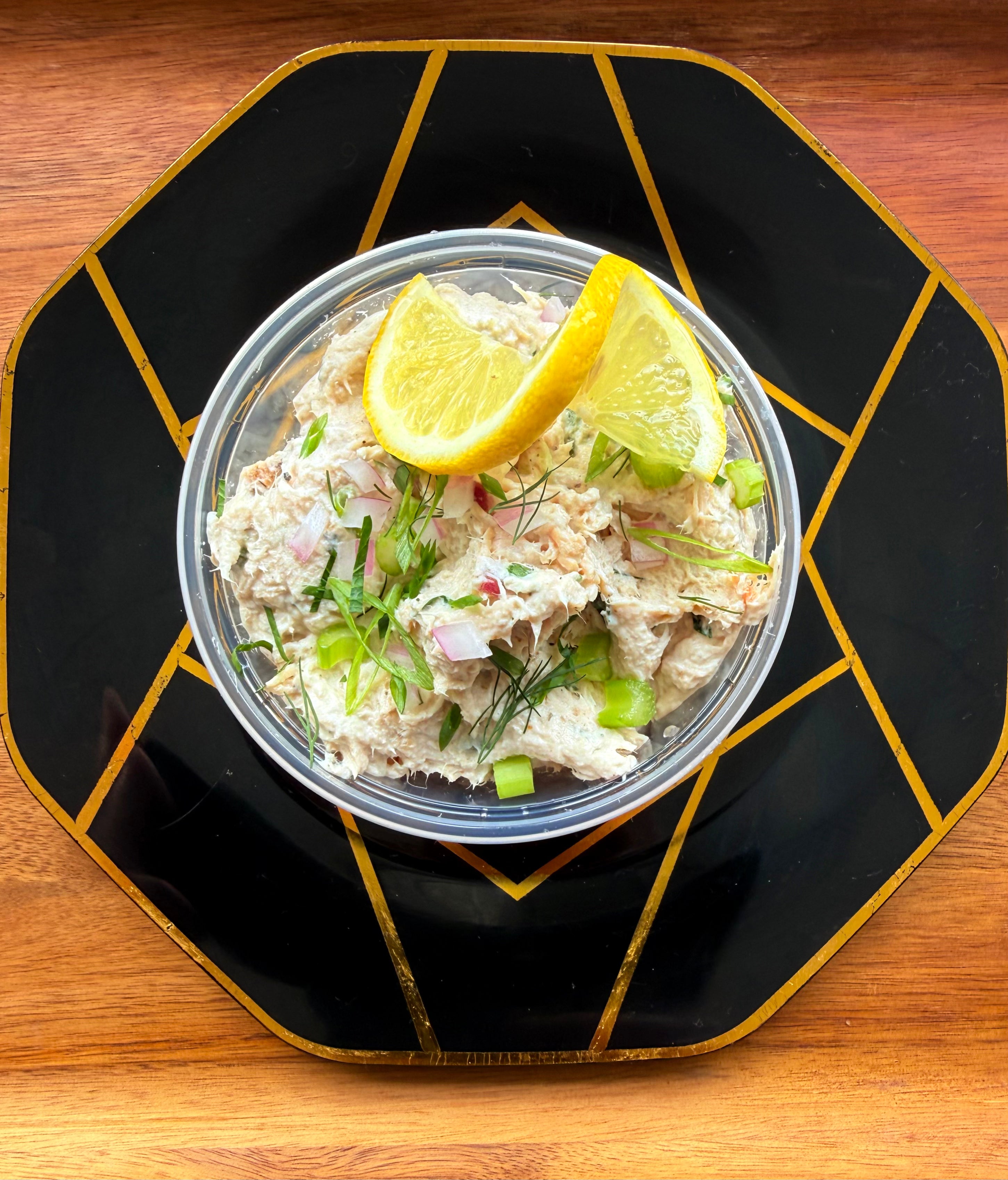 Munley Made Meals signature chicken salad with celery, red onion, and fresh dill, topped with two lemon wedges in a clear
