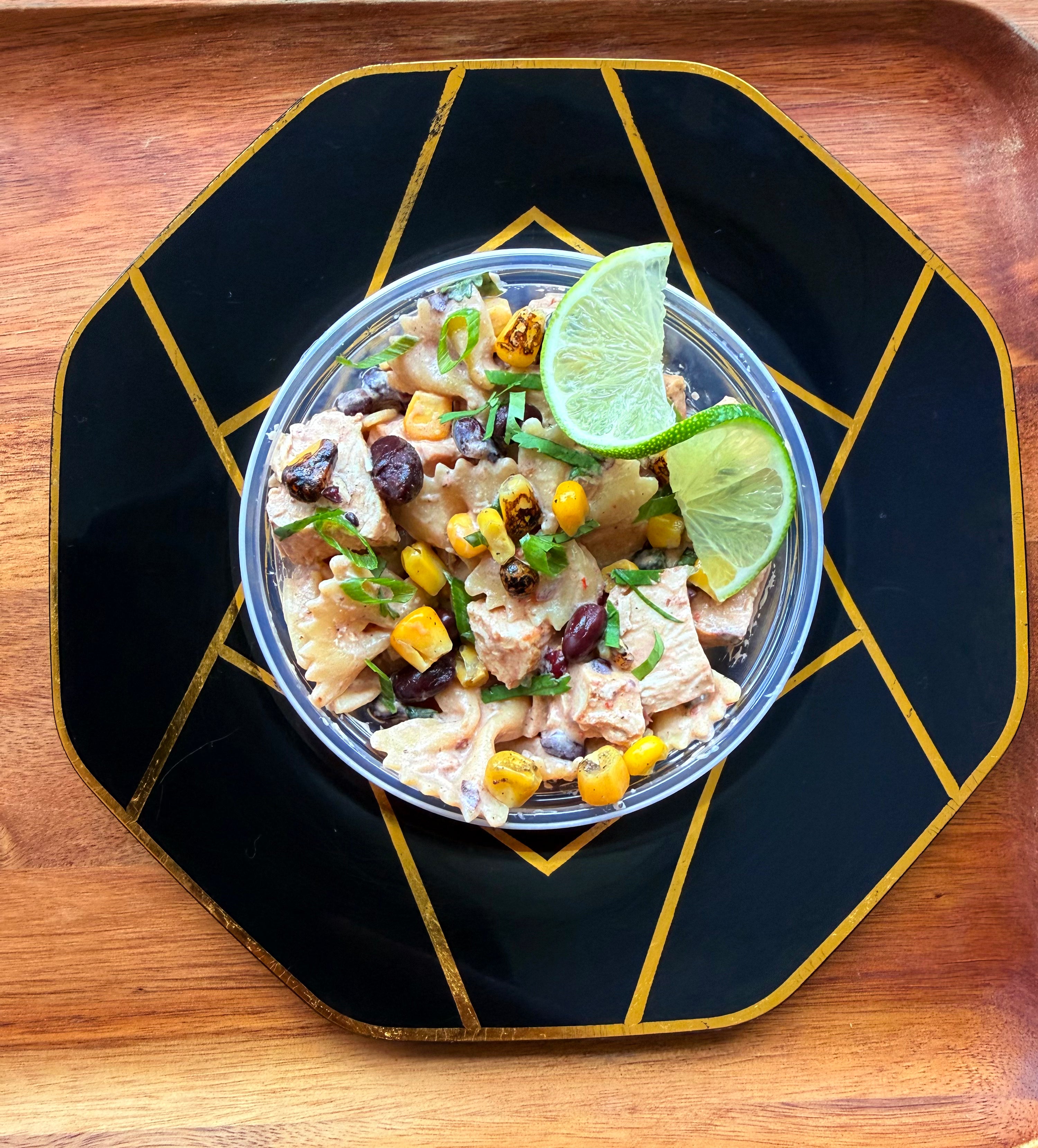 Southwest chicken pasta salad with black beans, corn, and cilantro in a clear bowl, garnished with a fresh lime wedge.