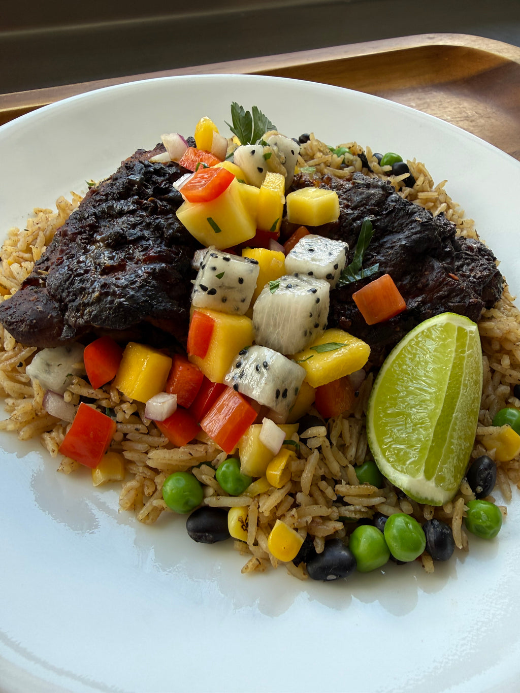 Jerk chicken over seasoned rice with black beans, peas, and tropical mango dragon fruit salsa, garnished with a lime wedge.