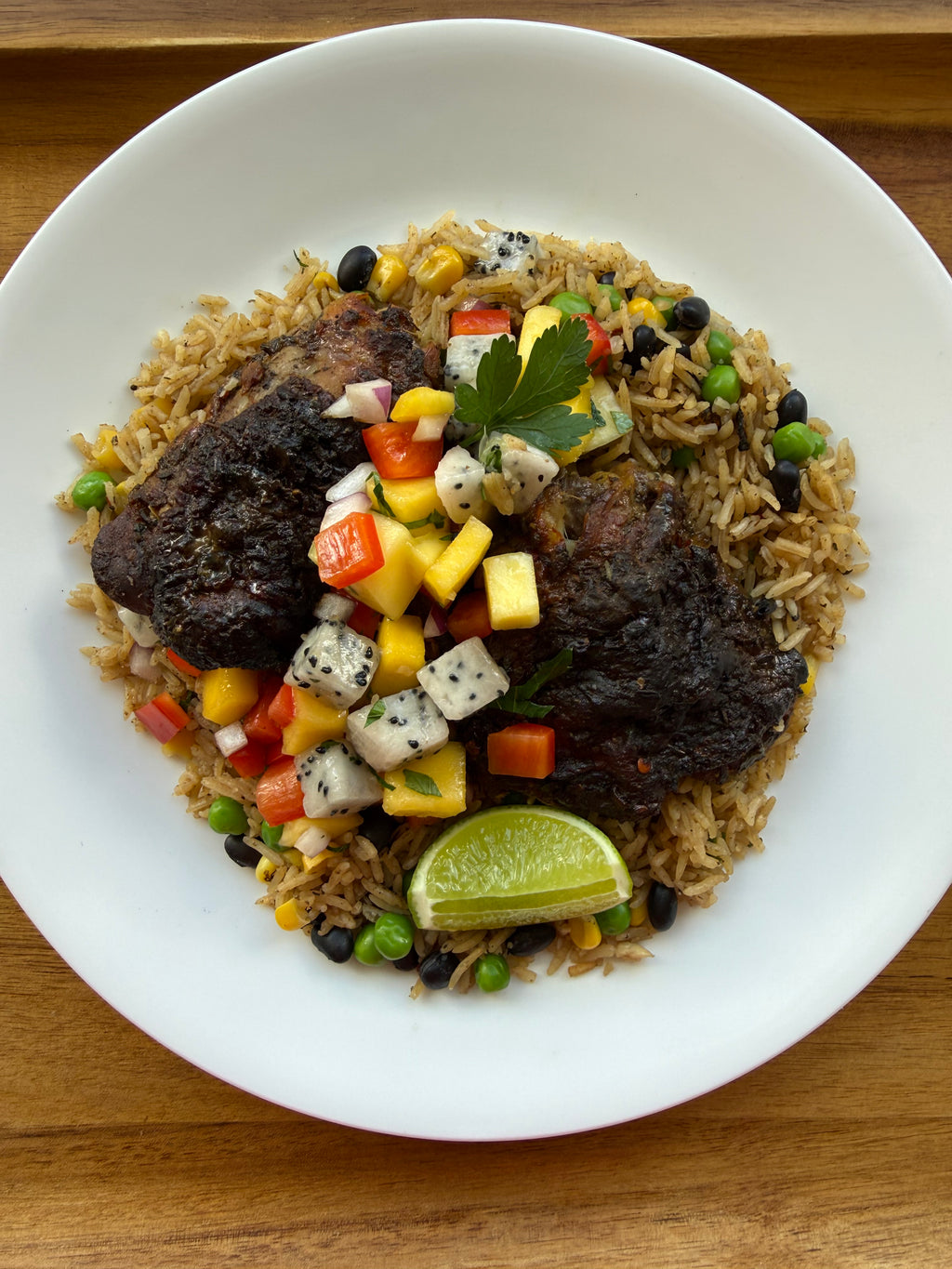 Jerk chicken thighs on seasoned rice with black beans, topped with mango dragon fruit salsa and a lime wedge.
